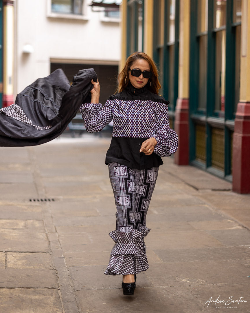 A woman wearing  Ankara top and trousers walking down the street and flying her coat