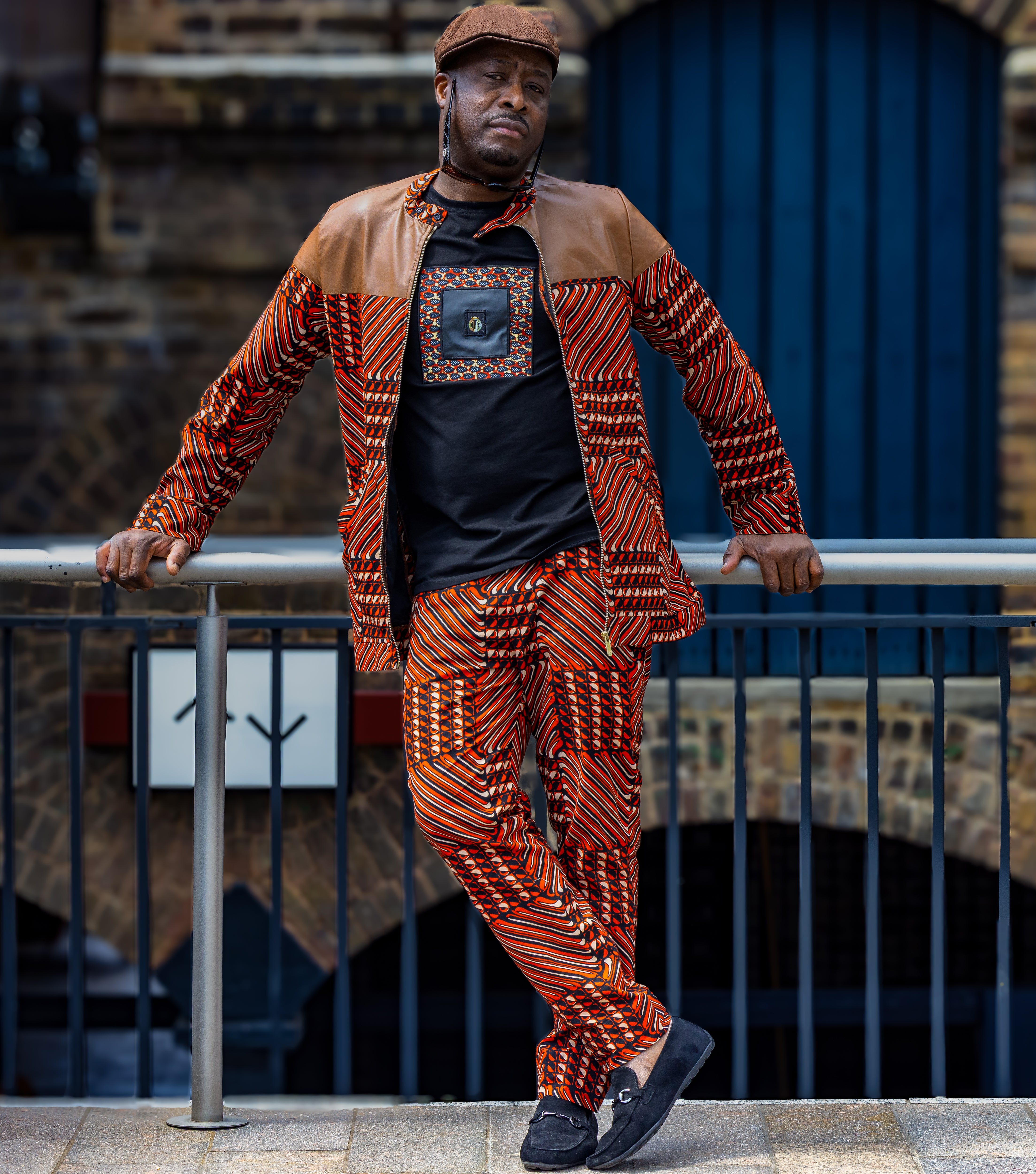 Man wearing a patterned African prints outfit standing against a railing with a building in the background