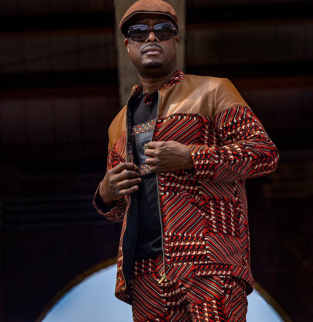 Man wearing a patterned African print jacket and sunglasses against a dark background